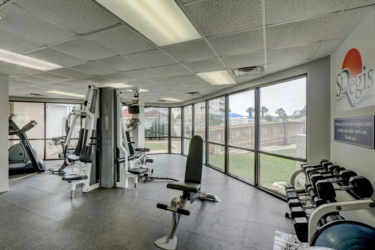 A bright, airy fitness center with modern exercise machines and free weights, featuring large windows that allow in plenty of natural light. The inviting setup includes ample space for solo or group workouts.