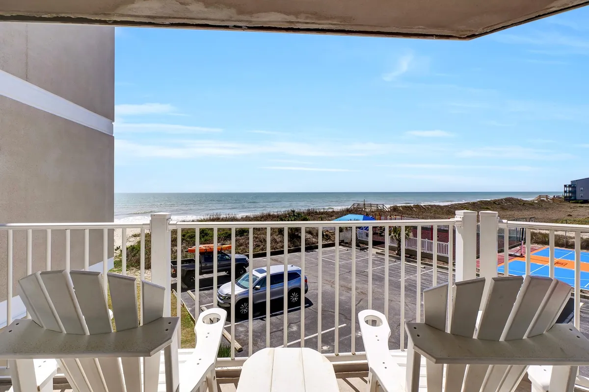 On the private balcony, comfortable chairs are set up for relaxing while gazing out at the expansive blue ocean and bright sky. The tranquil scene captures the essence of enjoying the sea breeze and spectacular views.