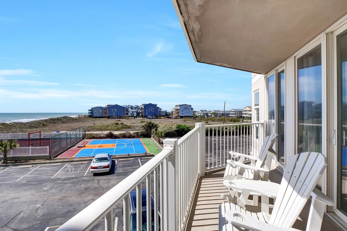 This image captures a serene balcony overlooking a colorful basketball court with the ocean in the background, as well as vacation homes nearby. The scene blends leisure with the tranquil energy of the seaside, connecting indoor living and productive work breaks with rejuvenating outdoor views.