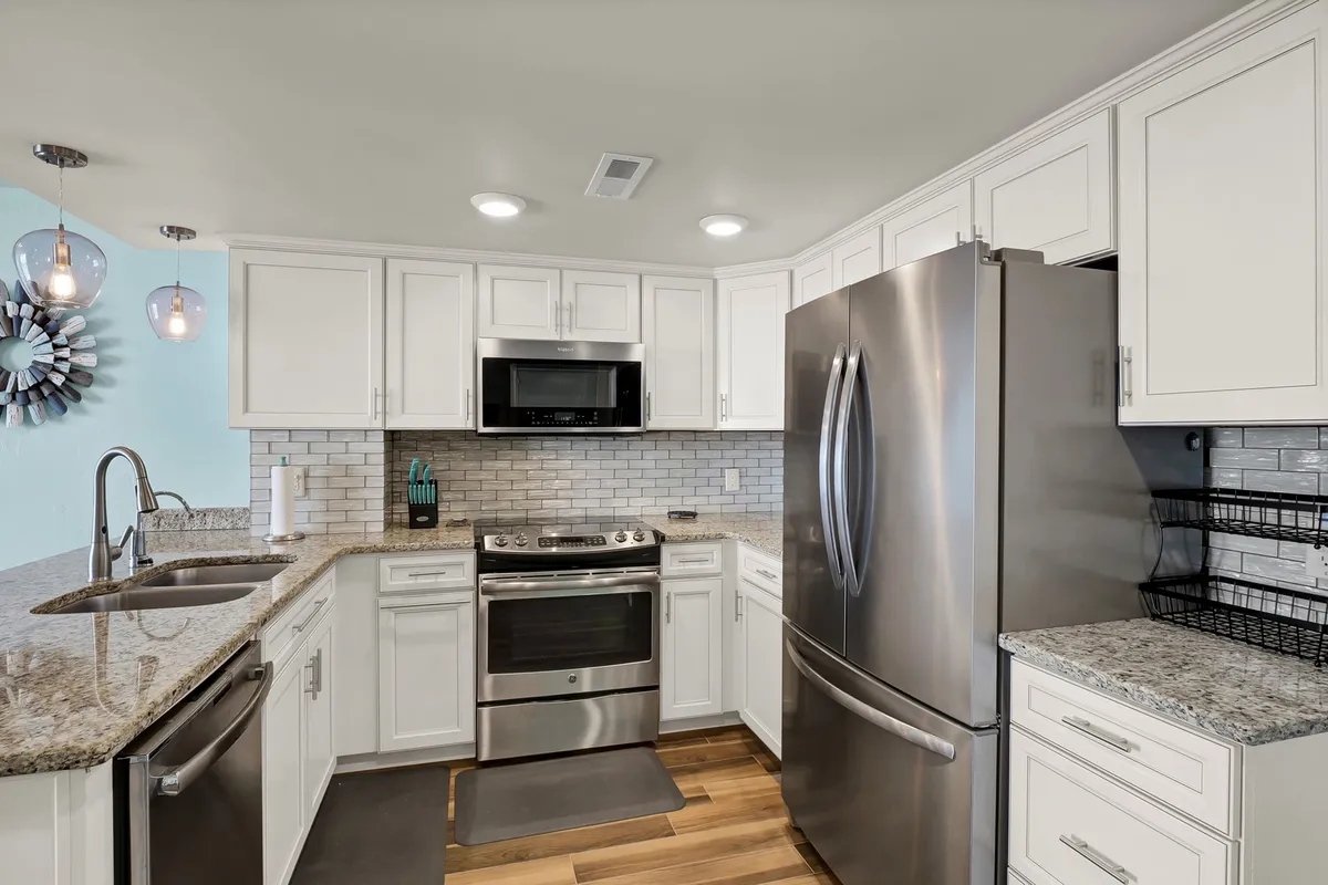 A contemporary kitchen featuring stainless steel appliances, sleek granite countertops, crisp white cabinetry, modern pendant lighting, and a classic subway tile backsplash. The space is well-lit and inviting, with plenty of room for meal preparation and entertaining.