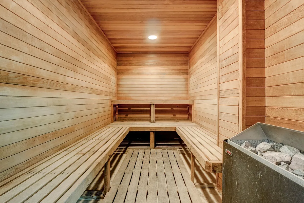 A tranquil sauna space with wooden benches and a stone heater, inviting relaxation, socializing, and wellness routines. The minimalist design and calming mood offer a perfect spot for unwinding after a productive day.