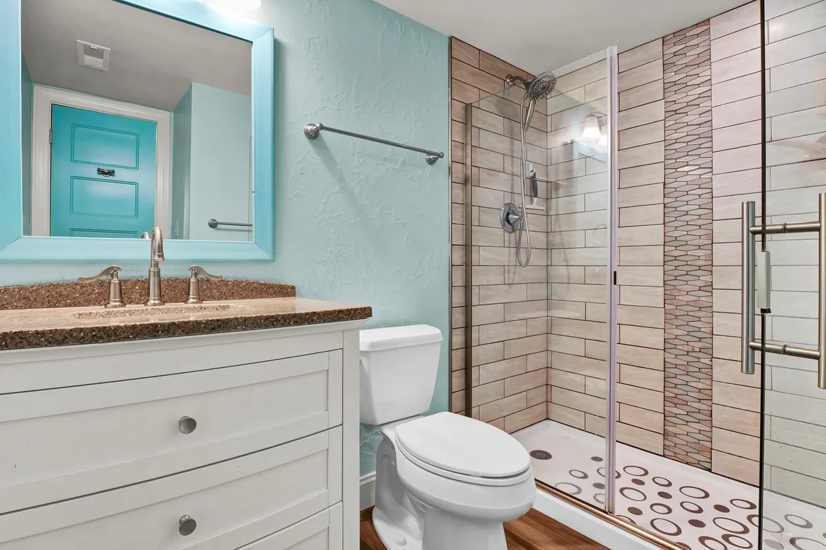 A bright, inviting bathroom with a blue-framed vanity mirror, granite countertop, and a shower with striking patterned tiles. The space feels airy and spa-like, perfect for unwinding after a long day.