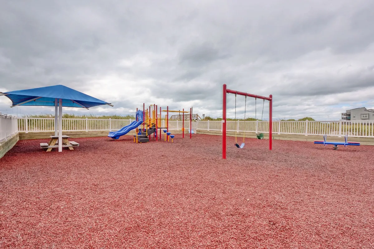 A cheerful outdoor playground features swings and play structures with a picnic area nearby. The space is designed for children’s recreation and family gatherings, set against a backdrop of greenery.